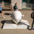 Bookhead Egghead shot in front of library at UC Davis with students, in blur, walking by